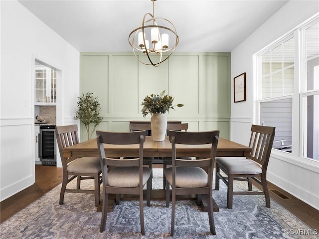 dining space with dark hardwood / wood-style floors, wine cooler, and an inviting chandelier