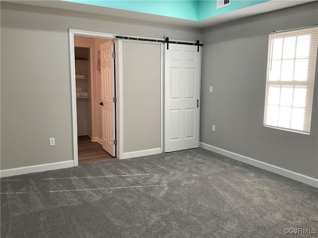 unfurnished bedroom with a closet, dark carpet, and a barn door