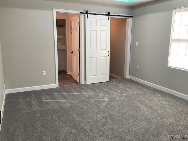 unfurnished bedroom with a barn door, dark carpet, a closet, and a spacious closet