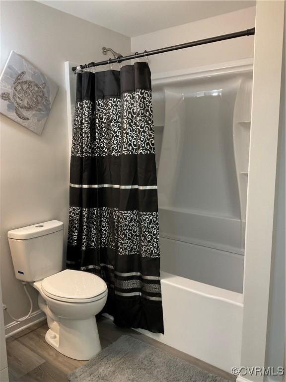 bathroom with hardwood / wood-style floors, shower / bath combination with curtain, and toilet