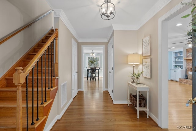 foyer featuring crown molding, ceiling fan with notable chandelier, a fireplace, and light wood-type flooring