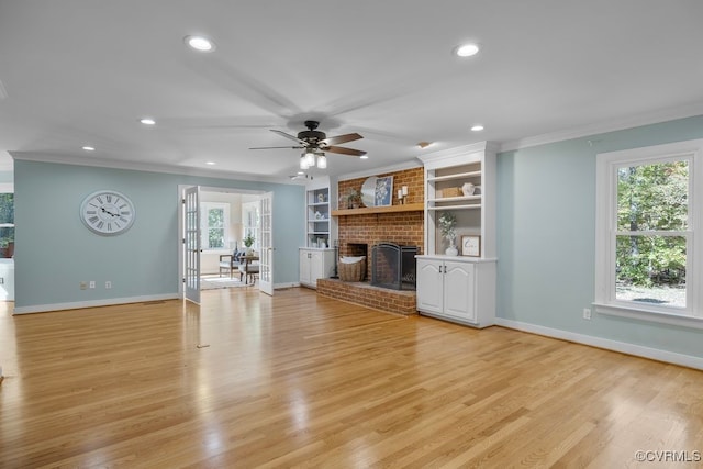 unfurnished living room featuring crown molding, a brick fireplace, light hardwood / wood-style flooring, built in features, and ceiling fan