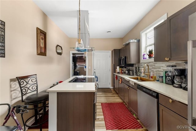 kitchen with dark brown cabinetry, sink, decorative light fixtures, appliances with stainless steel finishes, and a kitchen island