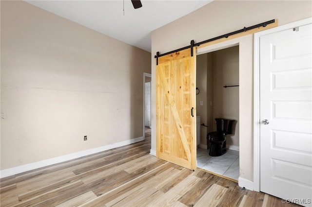 unfurnished bedroom featuring ensuite bath, a barn door, baseboards, and light wood-style flooring