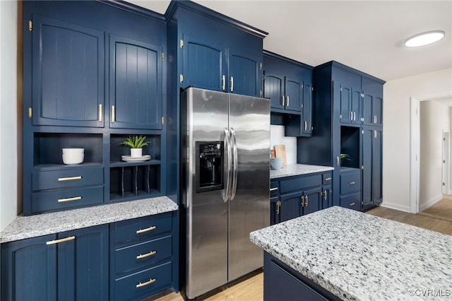 kitchen with blue cabinetry, light stone countertops, stainless steel fridge with ice dispenser, and light hardwood / wood-style flooring