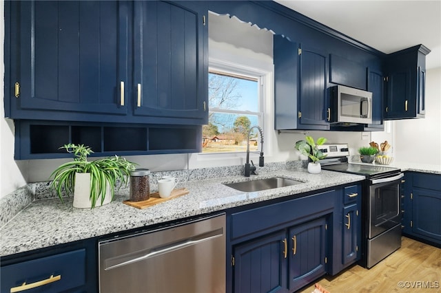 kitchen with blue cabinetry, sink, appliances with stainless steel finishes, light stone countertops, and light hardwood / wood-style floors