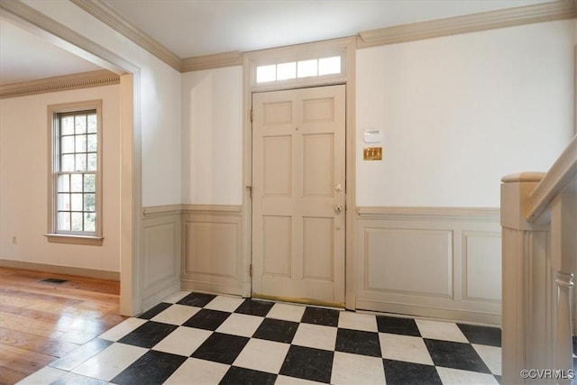 entrance foyer featuring dark floors, a wainscoted wall, visible vents, a decorative wall, and ornamental molding