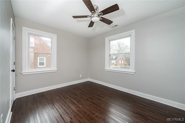 empty room with dark hardwood / wood-style floors, a wealth of natural light, and ceiling fan