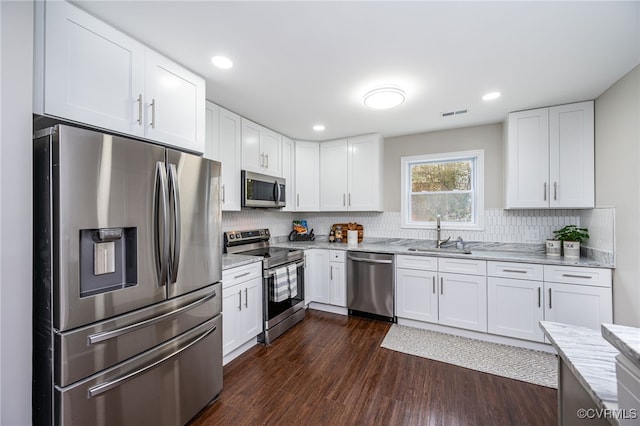 kitchen with sink, white cabinetry, light stone counters, appliances with stainless steel finishes, and dark hardwood / wood-style floors