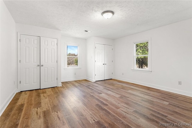 unfurnished bedroom with multiple windows, hardwood / wood-style floors, a textured ceiling, and multiple closets