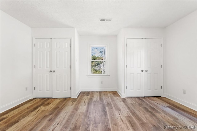 unfurnished bedroom with a textured ceiling, light hardwood / wood-style flooring, and two closets