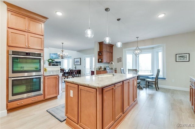 kitchen with pendant lighting, sink, a kitchen island with sink, and double oven