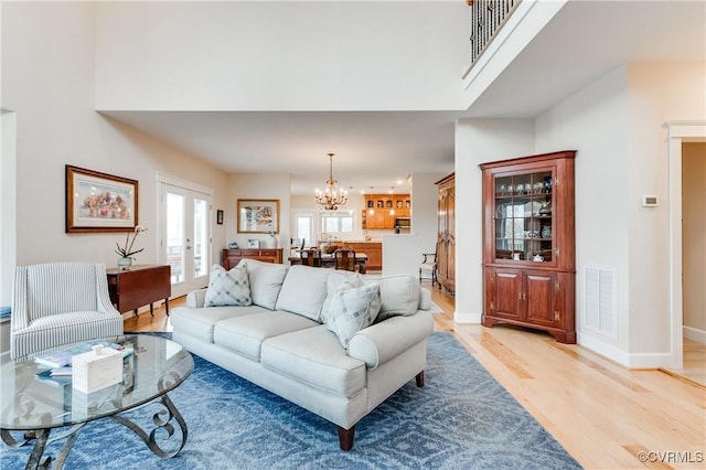 living room with a high ceiling, light hardwood / wood-style flooring, a notable chandelier, and french doors