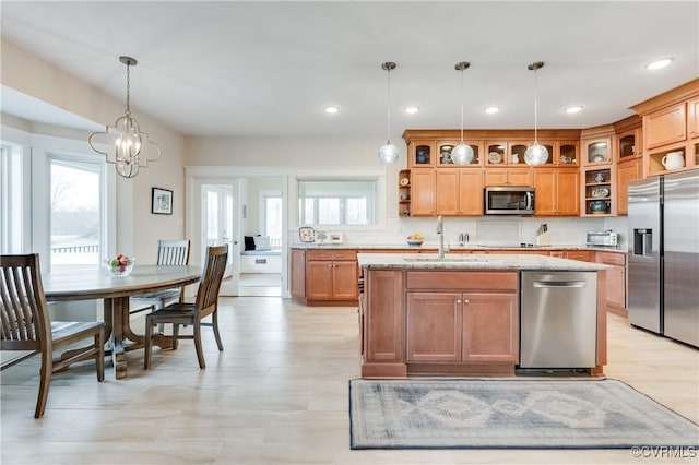 kitchen with sink, hanging light fixtures, stainless steel appliances, light stone countertops, and a kitchen island with sink