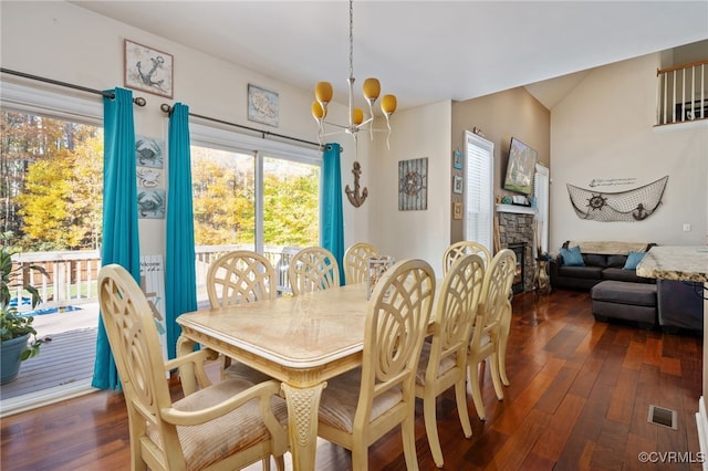 dining area featuring dark wood-type flooring, a chandelier, vaulted ceiling, and a stone fireplace