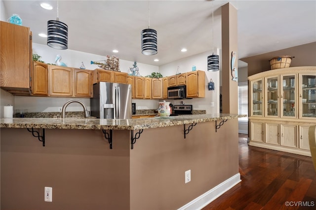 kitchen featuring kitchen peninsula, light stone countertops, sink, appliances with stainless steel finishes, and a kitchen breakfast bar