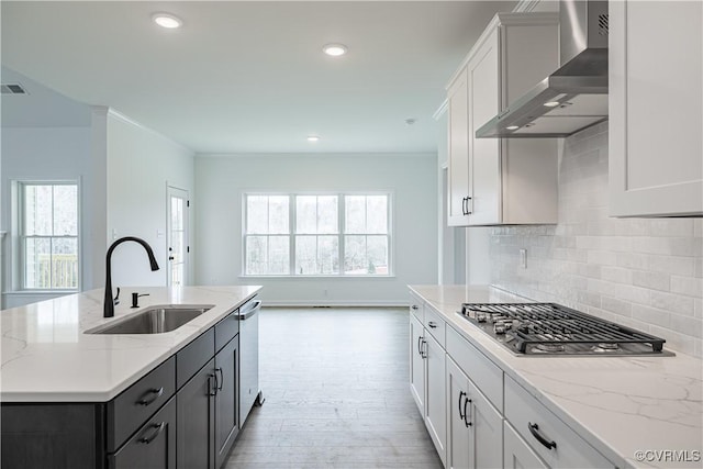 kitchen with sink, light stone counters, a center island with sink, wall chimney range hood, and white cabinets