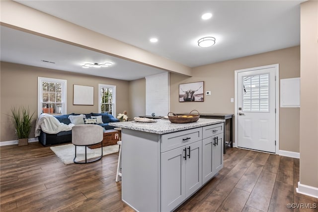 kitchen with a center island, dark wood-type flooring, light stone counters, and a breakfast bar