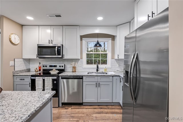 kitchen with appliances with stainless steel finishes, sink, white cabinets, and light stone counters