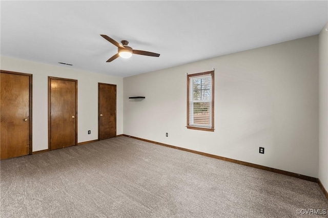 unfurnished bedroom featuring ceiling fan, carpet, and two closets