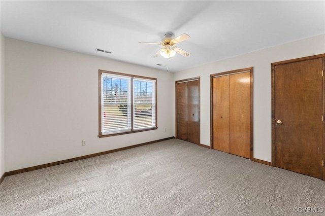 unfurnished bedroom with two closets, light colored carpet, and ceiling fan