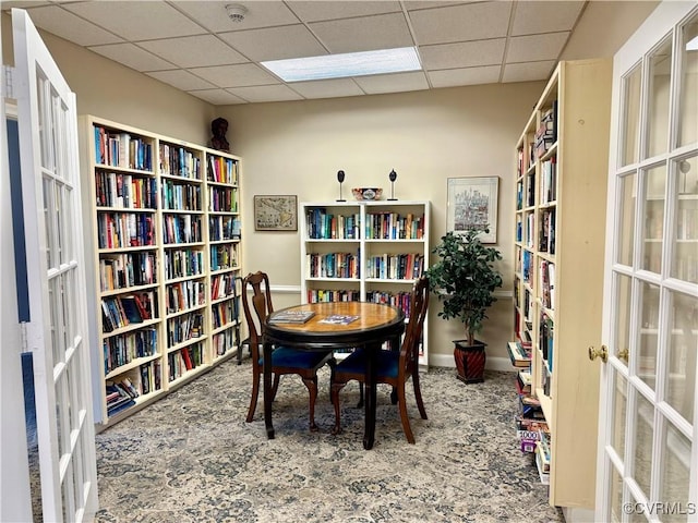 office area featuring carpet flooring, a paneled ceiling, and wall of books