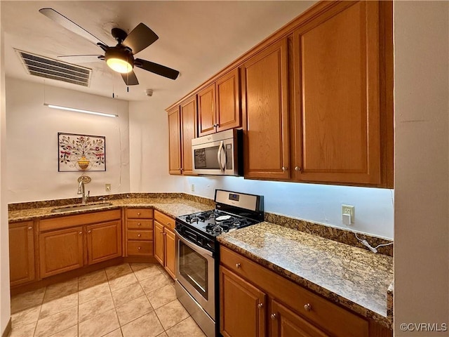 kitchen with visible vents, a sink, dark stone counters, appliances with stainless steel finishes, and brown cabinetry