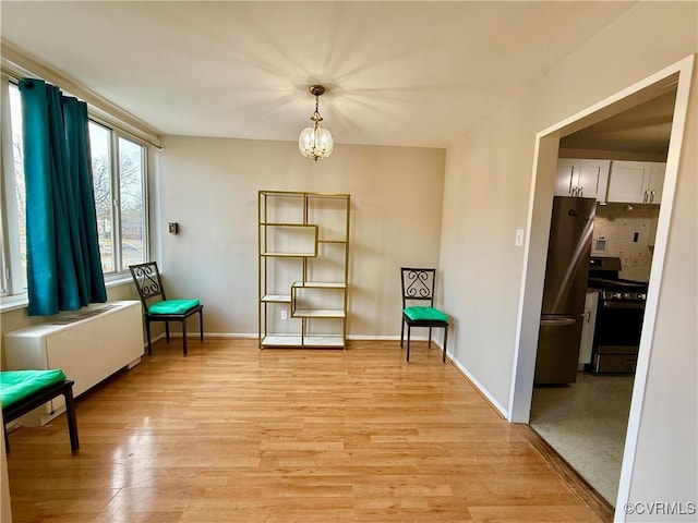 sitting room featuring light wood-type flooring, baseboards, a notable chandelier, and radiator heating unit