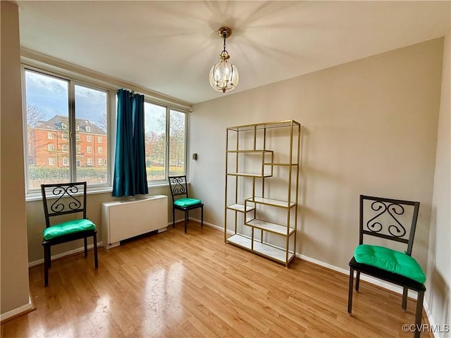 living area featuring baseboards, light wood-style floors, an inviting chandelier, and radiator heating unit