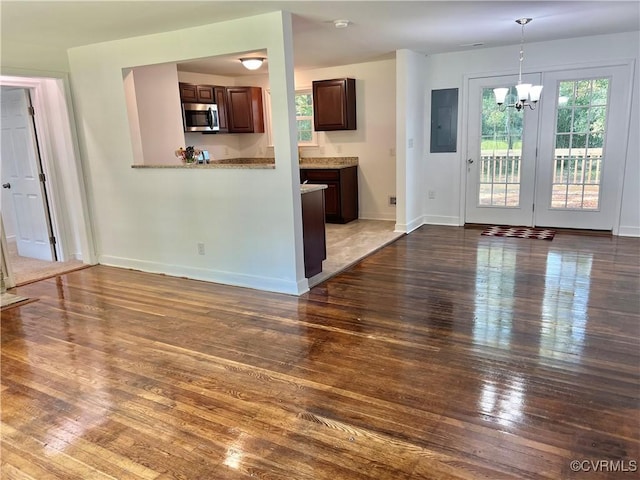 unfurnished living room featuring dark hardwood / wood-style flooring, electric panel, and a chandelier