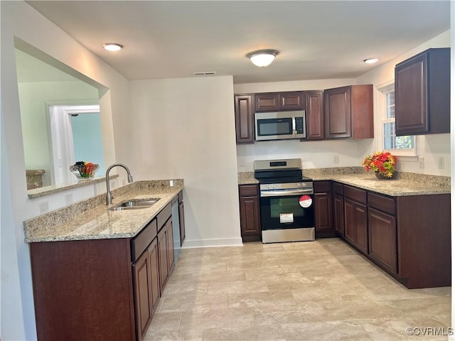 kitchen with sink, appliances with stainless steel finishes, dark brown cabinets, light stone countertops, and kitchen peninsula