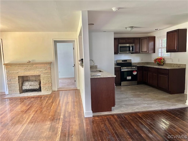 kitchen featuring sink, appliances with stainless steel finishes, hardwood / wood-style floors, dark brown cabinets, and a fireplace