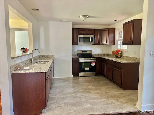 kitchen featuring light stone counters, dark brown cabinetry, appliances with stainless steel finishes, and sink