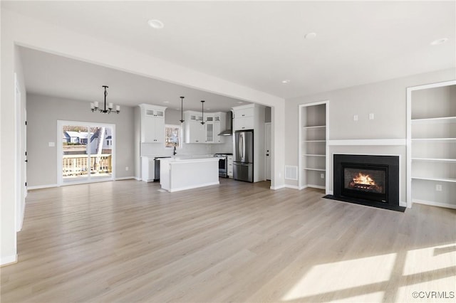 unfurnished living room with a notable chandelier, light hardwood / wood-style floors, and built in shelves