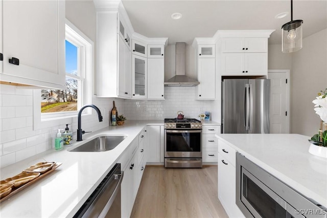 kitchen featuring wall chimney exhaust hood, sink, decorative light fixtures, stainless steel appliances, and white cabinets