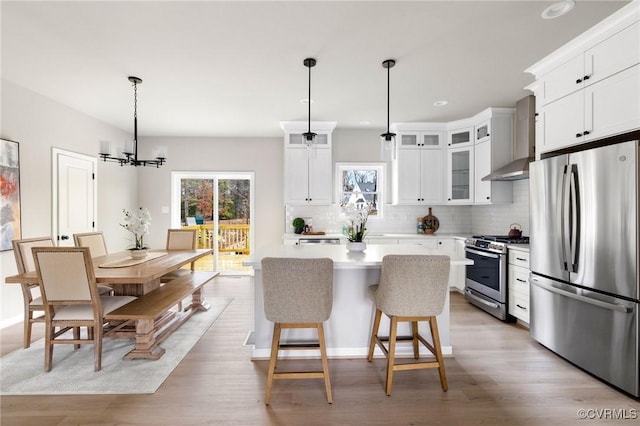 kitchen with white cabinetry, decorative light fixtures, appliances with stainless steel finishes, a kitchen island, and wall chimney range hood