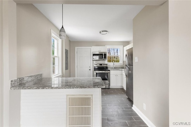 kitchen featuring white cabinetry, light stone counters, decorative light fixtures, appliances with stainless steel finishes, and kitchen peninsula