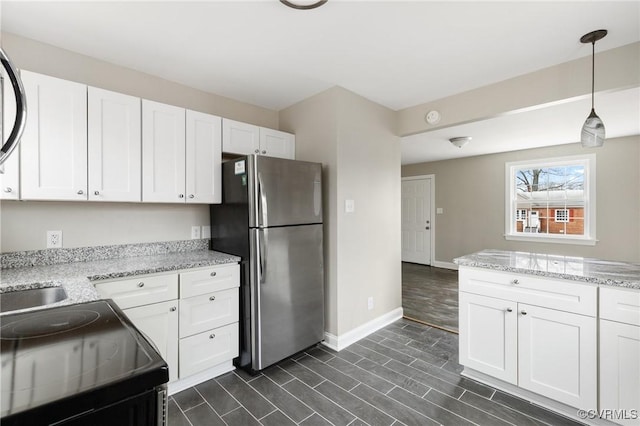 kitchen with stainless steel refrigerator, black / electric stove, pendant lighting, light stone countertops, and white cabinets