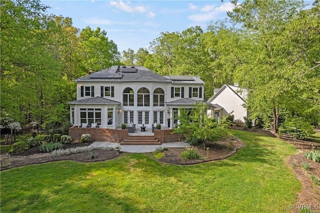 rear view of house with a yard, a chimney, a sunroom, and roof mounted solar panels