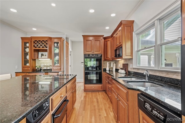 kitchen featuring brown cabinetry, glass insert cabinets, dark stone countertops, black appliances, and a sink