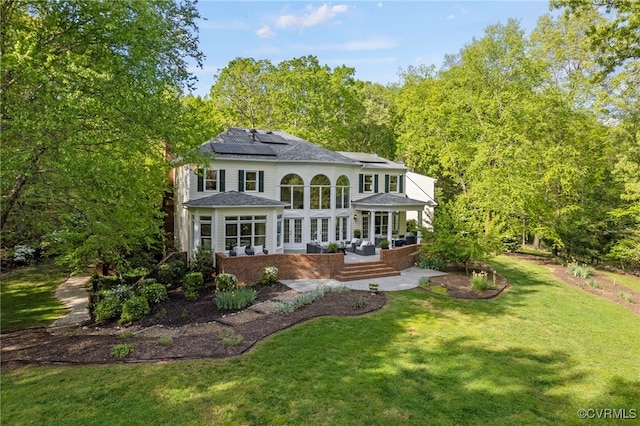 back of property featuring solar panels, a lawn, and a sunroom