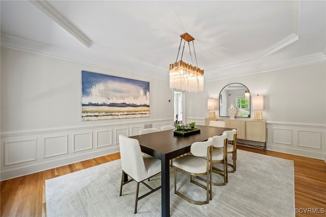 dining area featuring light wood-style flooring, a decorative wall, a notable chandelier, ornamental molding, and wainscoting