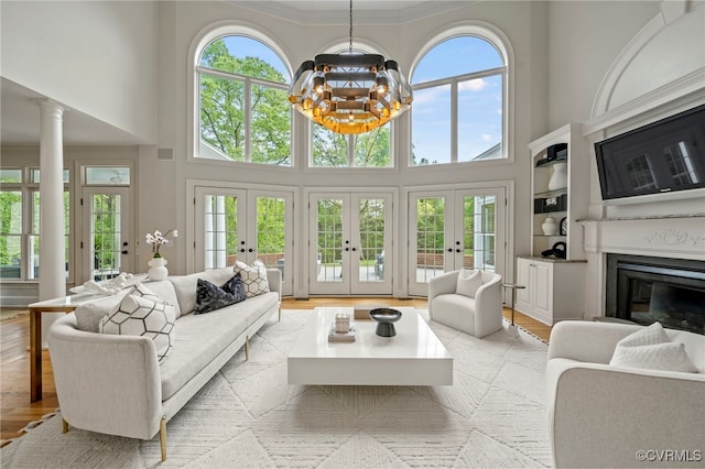 living area with a chandelier, a glass covered fireplace, french doors, and light wood finished floors