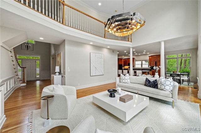 living area with decorative columns, a towering ceiling, light wood-style flooring, ornamental molding, and a notable chandelier