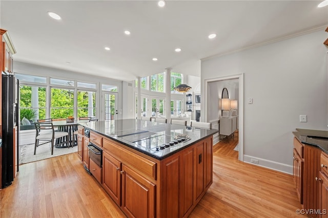 kitchen featuring light wood-type flooring, a center island, dark stone counters, black appliances, and brown cabinetry