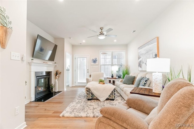 living room with a ceiling fan, light wood-type flooring, a glass covered fireplace, and baseboards