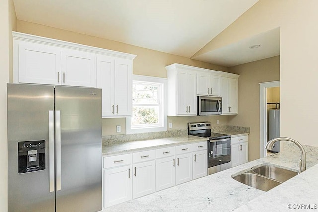 kitchen with lofted ceiling, sink, white cabinets, stainless steel appliances, and light stone countertops