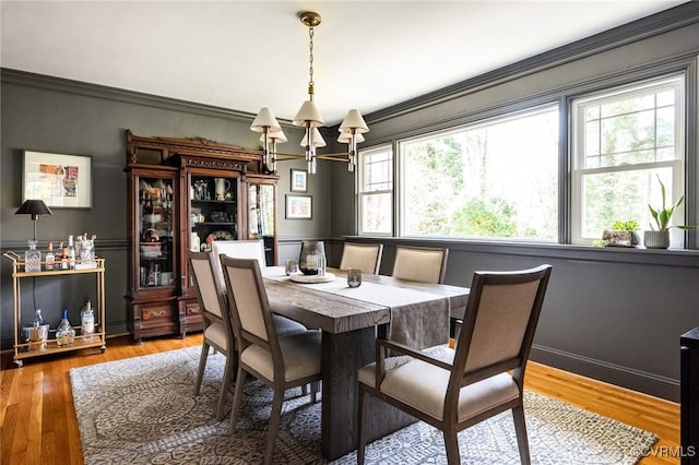 dining space with hardwood / wood-style flooring, ornamental molding, and a notable chandelier