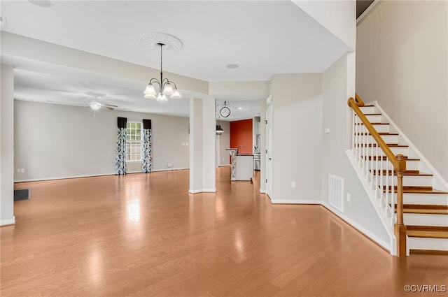 unfurnished living room featuring ceiling fan with notable chandelier and light hardwood / wood-style floors