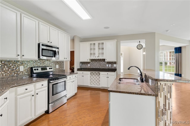 kitchen with sink, light wood-type flooring, an island with sink, stainless steel appliances, and white cabinets